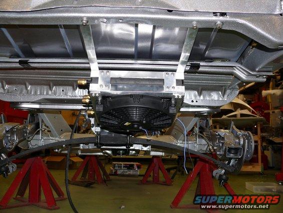 Undercarriage of a vehicle on jack stands, showing a cooling fan and leaf spring suspension