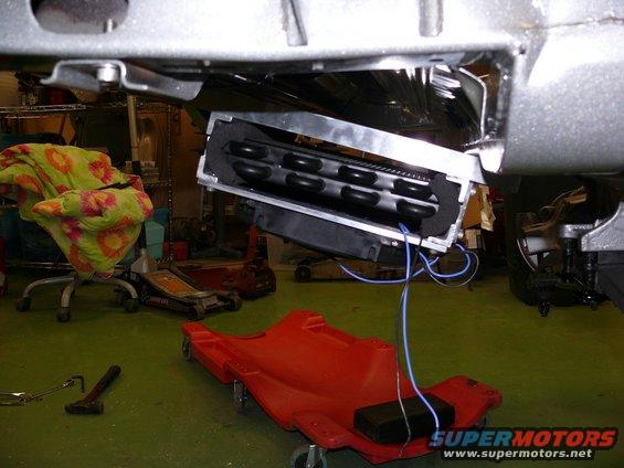 Car's undercarriage with an exposed HVAC unit and wiring, resting on a red creeper