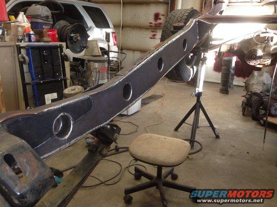 Vehicle frame on jack stands in a workshop with a silver SUV in the background