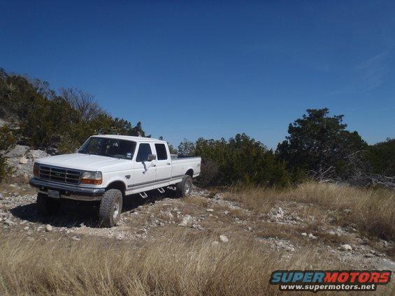 White 1997 Ford F-350 crew cab pickup truck parked on a rocky, grassy hill