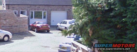 Red convertible parked in driveway, rear view. A white van is parked nearby