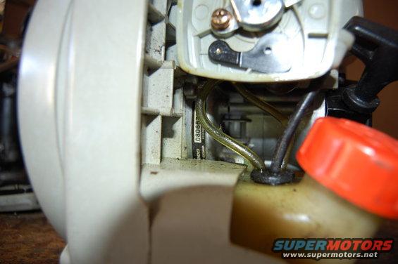 Close-up of a blower carburetor with a partially visible serial number and fuel lines