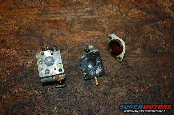 Two carburetor assemblies and a gasket on a wooden surface