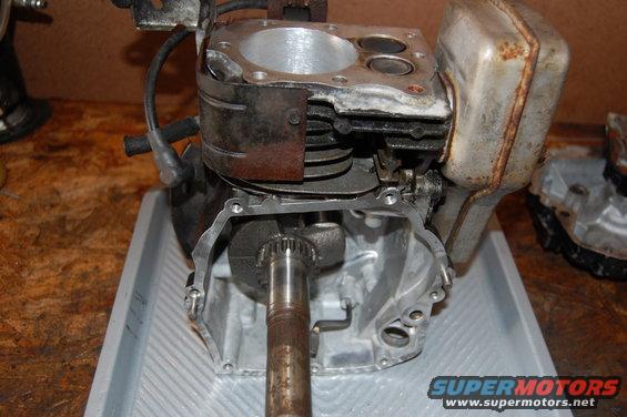Engine block with crankshaft and muffler. The engine is disassembled and sits on a gray tray