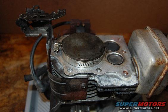 Engine cylinder head with piston and valves visible. Exhaust muffler attached