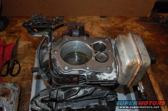 Engine cylinder head with valves visible, next to a muffler. Scissors and a red cloth are on the left