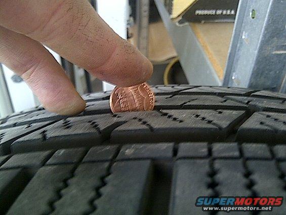 Tire tread depth measured with a penny, showing tread is low