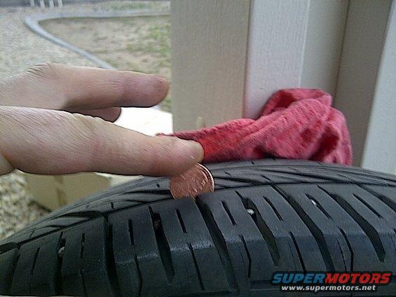 Penny in tire tread, showing shallow depth. Red cloth and hand visible