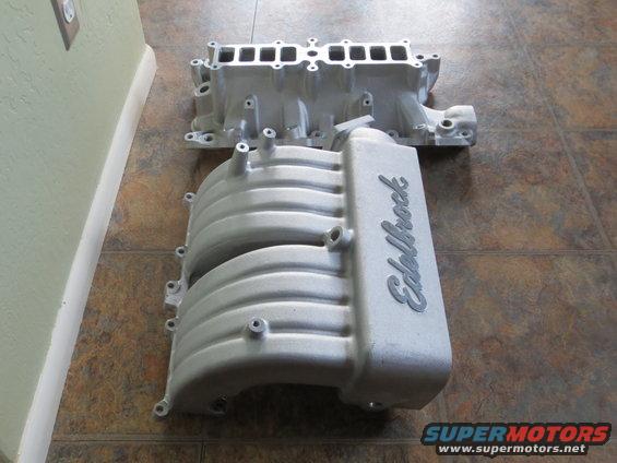 Two aluminum intake manifolds, one labeled Edelbrock, on a tiled floor