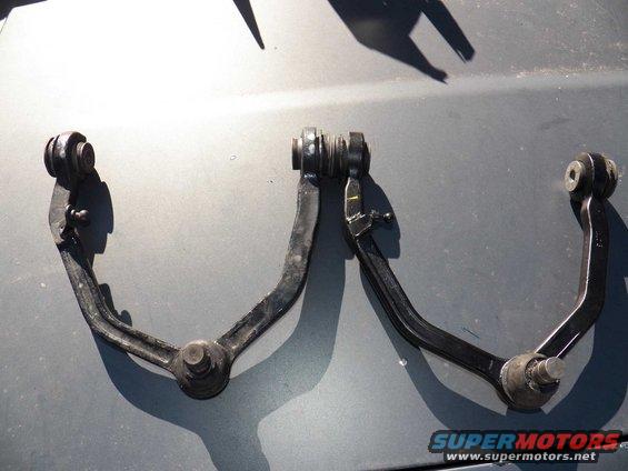 Two black front suspension control arms on a gray surface