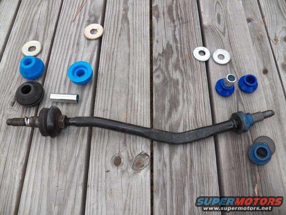 Suspension stabilizer bar with new blue bushings and washers laid out on wooden planks