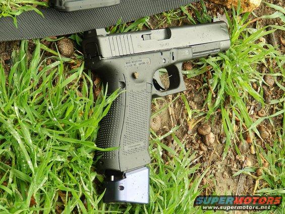 Pistol with extended magazine lying on grass. Text on slide reads 'GLOCK INC. SMYRNA . GA.'