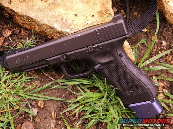 Glock pistol with extended magazine resting on grass and dirt next to a rock