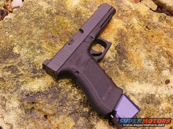 Black Glock pistol with extended purple magazine on a rock