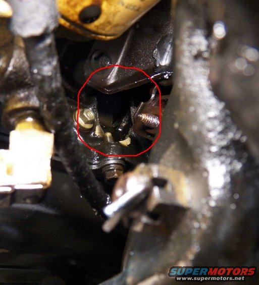 Close-up of engine components with a red circle highlighting a bracket and bolt assembly