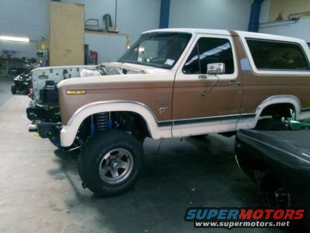 Brown and white Ford Bronco with hood removed, showing front suspension and engine bay