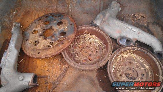 Flywheel, brake drums, and exhaust manifold parts are piled in a rusty metal container