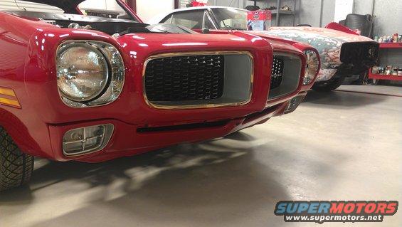 Red 1970s muscle car front end with hood open, another car behind it