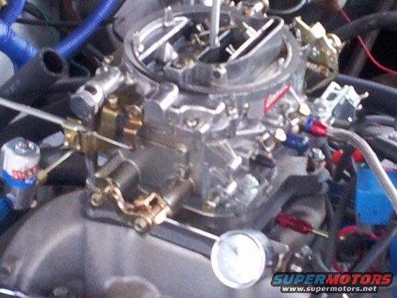Close-up of a chrome carburetor with red and blue fuel lines, and a small gauge