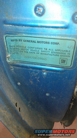 Close-up of a blue vehicle's VIN plate, showing "MFD. BY GENERAL MOTORS CORP."