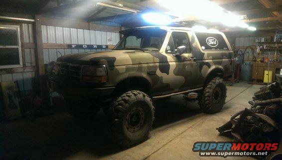 Camouflaged Ford Bronco parked in a garage with large tires