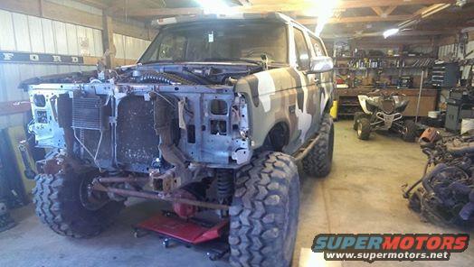Camouflaged Ford Bronco with front end removed, parked in a garage