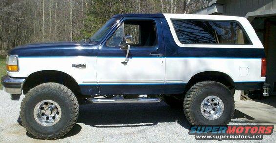 Side view of a lifted 1994 Ford Bronco with two-tone blue and white paint and large off-road tires