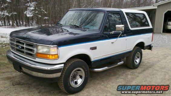 Two-tone blue and white Ford Bronco parked outside in a wooded area