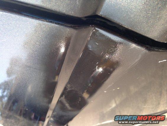 Gray metallic car body panel seam with black trim and visible scratches