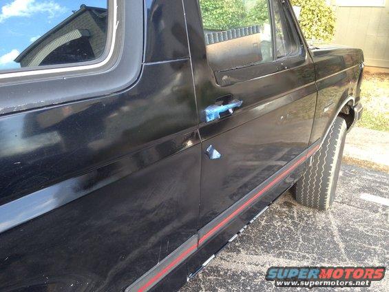Black 1987 Ford Bronco side view with red trim and blue tape on door handle