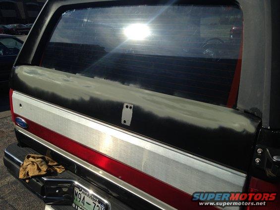 1990 Ford Bronco rear tailgate with primer and body filler applied, showing the Ford emblem and red stripe