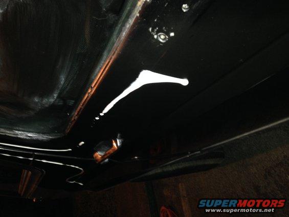 Underside of vehicle with white paint drips on black undercoating