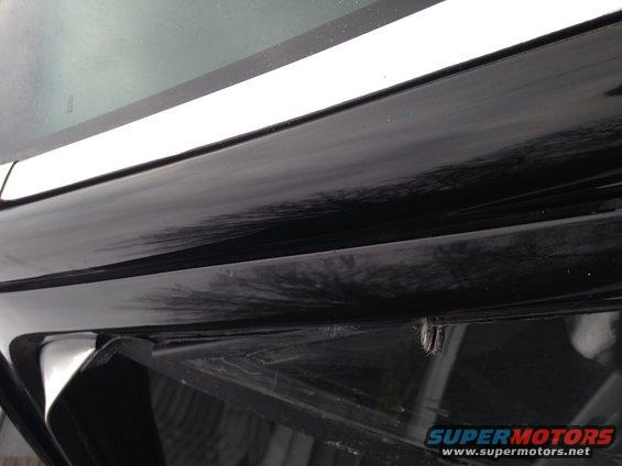 Black car door edge with a white trim piece above it. A small metal clip is visible