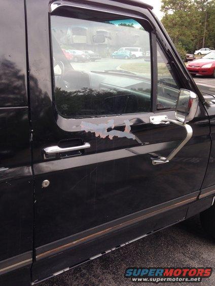Side view of a black SUV door with peeling paint near the handle and window trim. Other vehicles are visible in the background