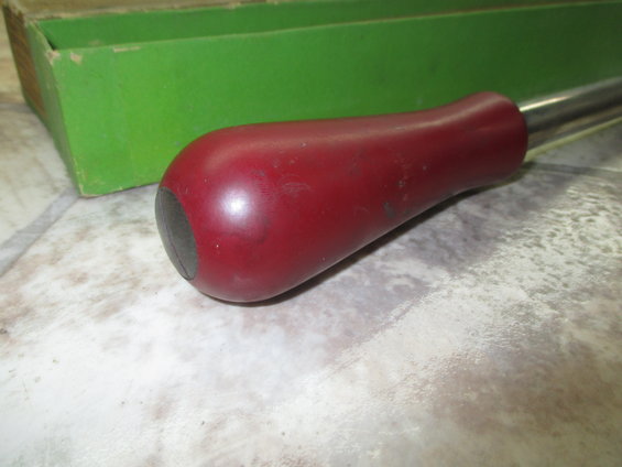 Red handle tool with metal shaft and black tip, next to a green box
