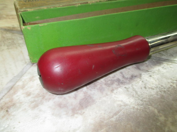 Red handle of a tool with a metal shaft, next to a green box
