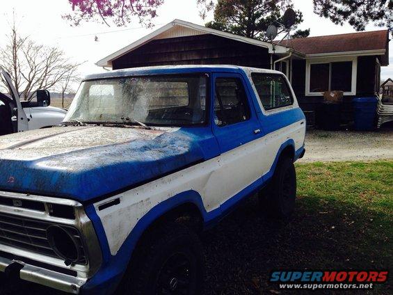Blue and white Ford Bronco parked in a yard with a house in the background