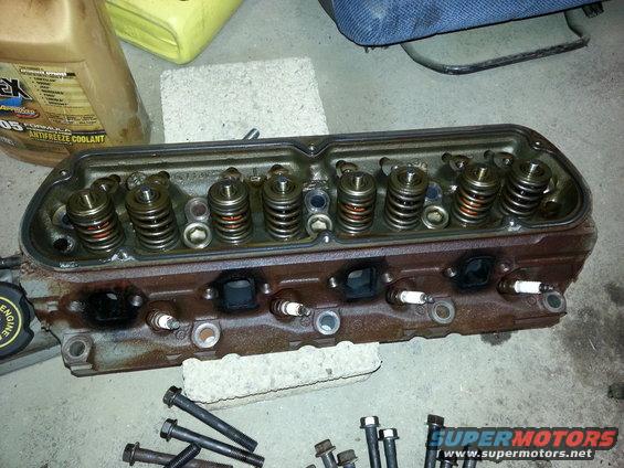 Engine cylinder head with spark plugs and valve springs. Bottle of antifreeze in background