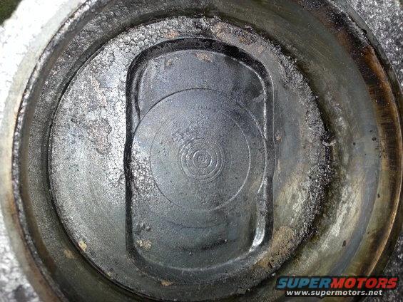 Close-up of a dirty engine cylinder head with carbon buildup and a circular valve seat