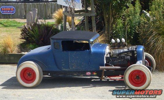 Blue hot rod car with exposed engine, red wheels, and white-wall tires, seen from the side