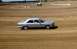 1969 Lincoln Continental - A silver sedan navigates a dirt track, with a water truck visible in the distance on a sunny day.