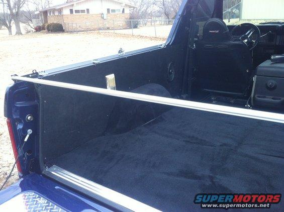 Blue pickup truck bed with black carpet and interior showing seats and steering wheel