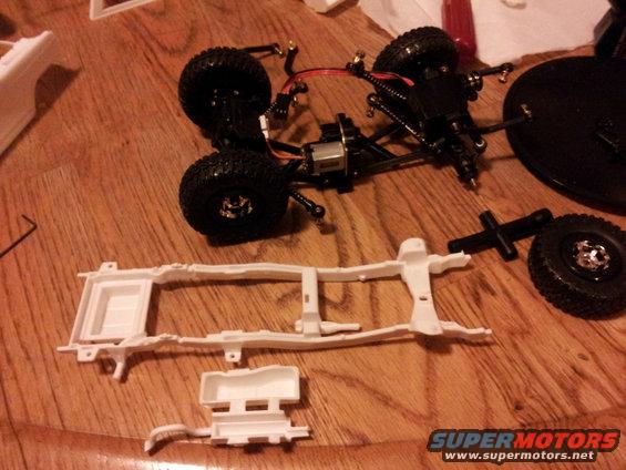 RC car chassis, motor, suspension, and wheels laid out on a wooden surface