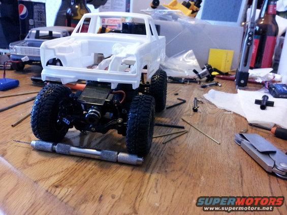 White model truck chassis with large tires and tools on a wooden surface