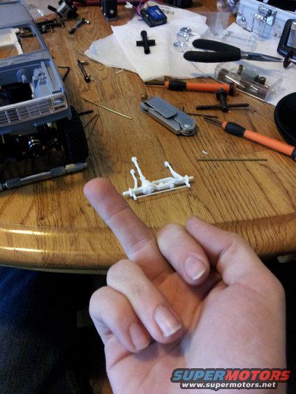 Hand holding a model car suspension part over a table with model car parts and tools