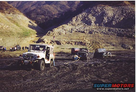 off-road vehicles stuck in mud, one being pulled by another