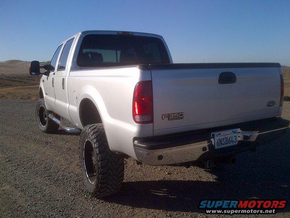Silver Ford F-350 pickup truck, lifted with large tires, parked on a dirt road