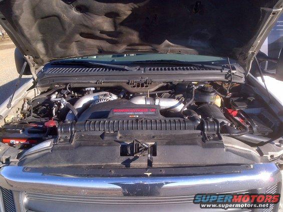 Truck engine bay with hood open, showing a V8 turbo diesel engine. Silver and black components are visible