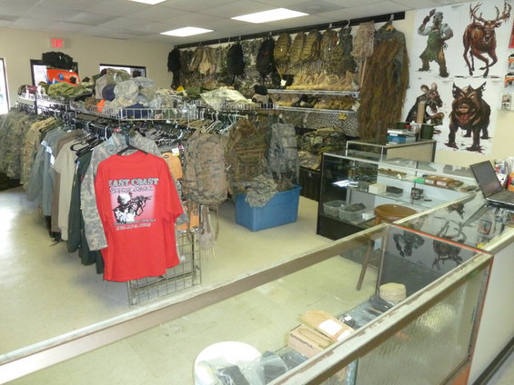 Interior of a store selling camouflage clothing, backpacks, and tactical gear, with a red t-shirt in the foreground