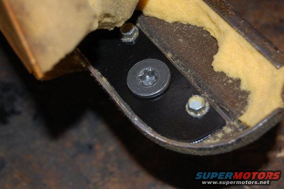 Close-up of a metal seat bracket with yellow foam padding, showing two hex bolts and one Torx bolt with a washer